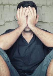 Depressed young man sitting on the floor and covering his face with a grunge wall background